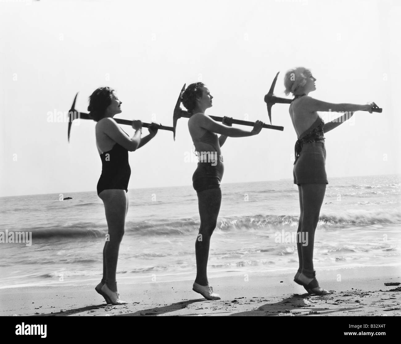 Drei Frauen posieren mit einer Axt holen am Strand Stockfoto