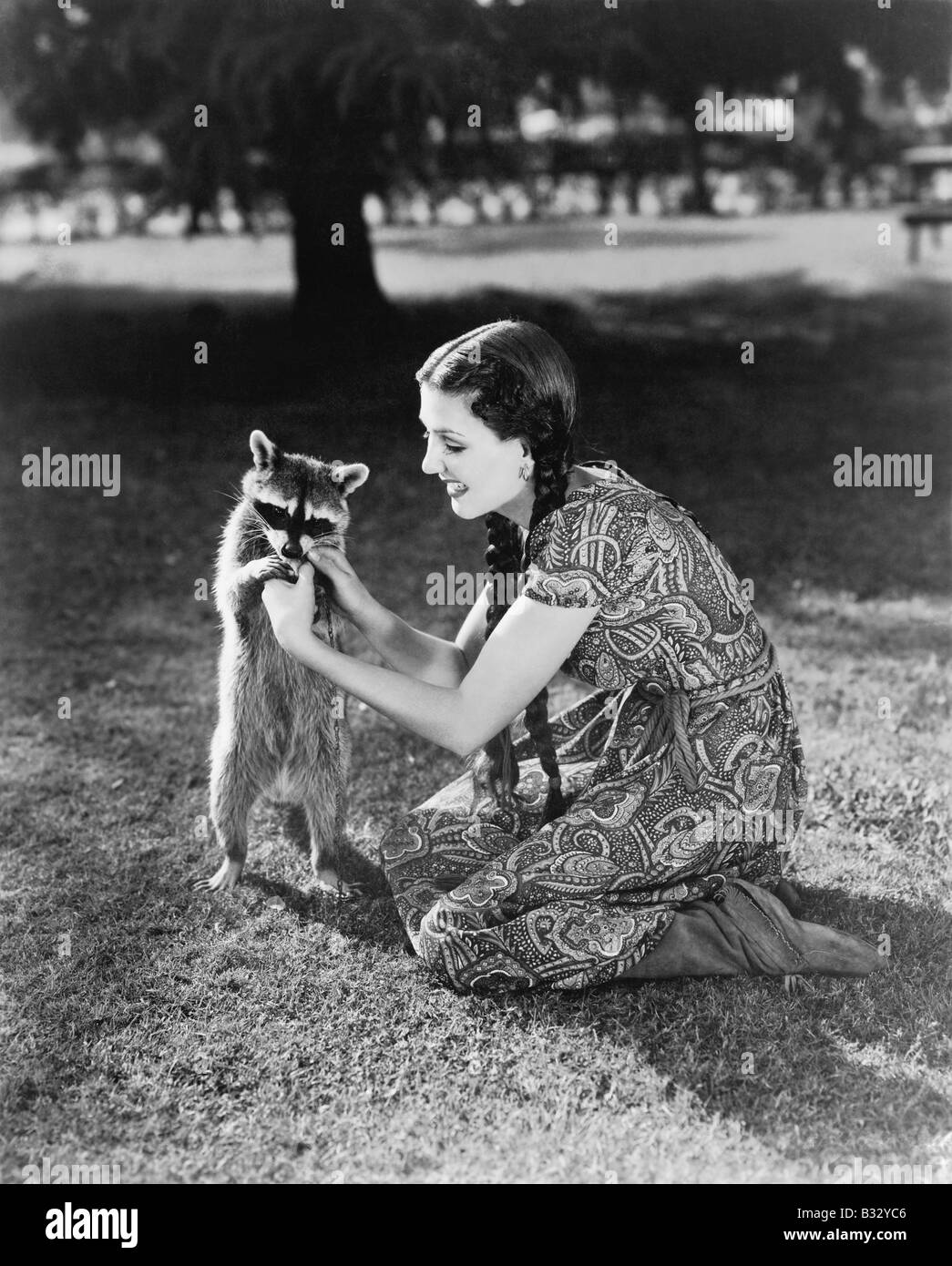 Frau kniend auf dem Rasen spielen mit einem zahmen Waschbär Stockfoto