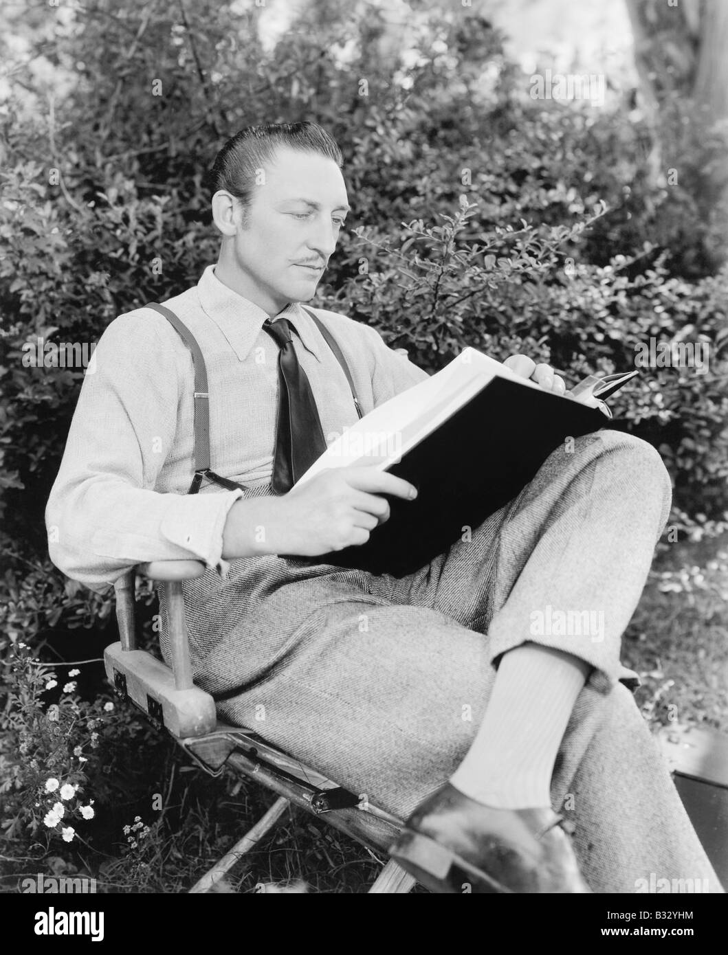 Mann sitzt in seinem Garten ein Buch lesen Stockfoto