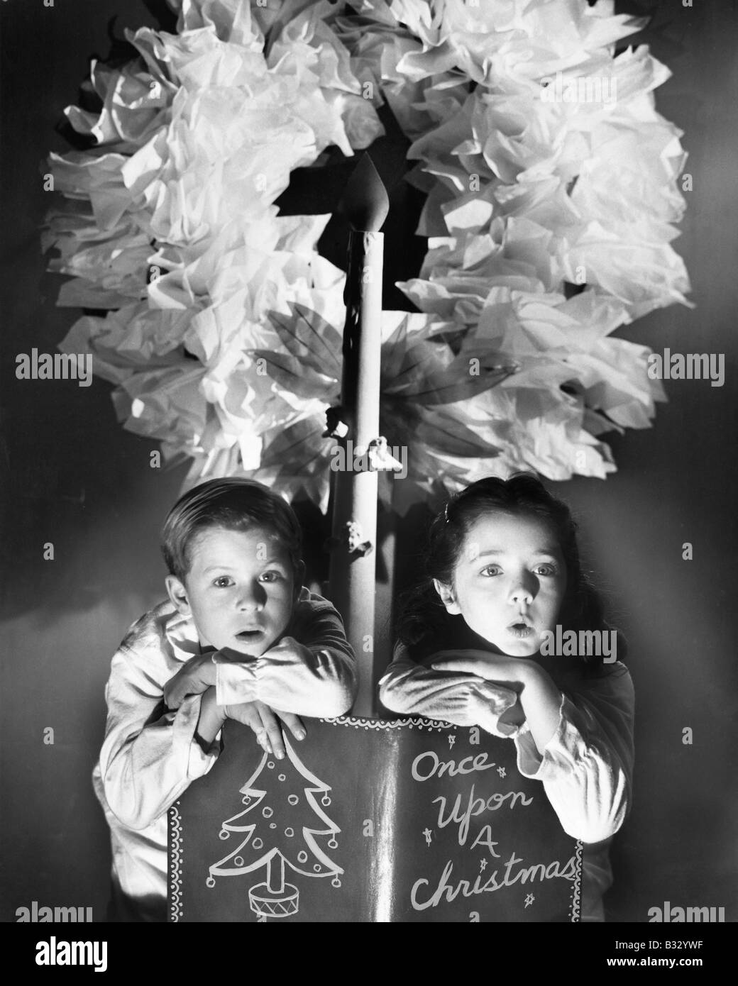 Zwei Kinder sitzen unter einem Kranz halten ein Weihnachts-Märchenbuch Stockfoto