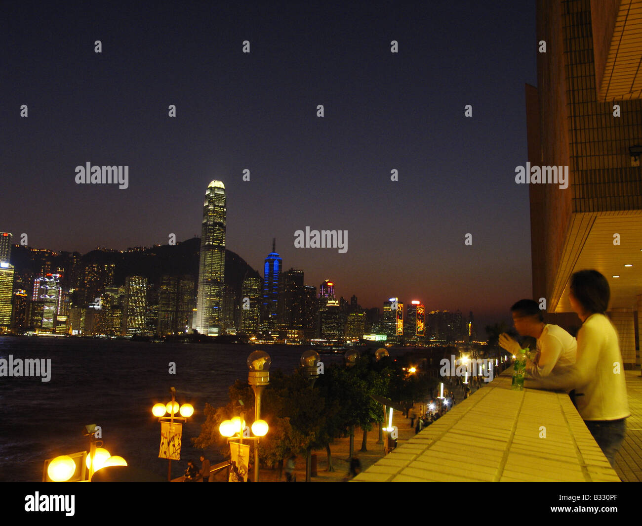 Männer suchen am Abend aus Kowloon auf Victoria Harbour und die Skyline Hongkongs Central District. Stockfoto