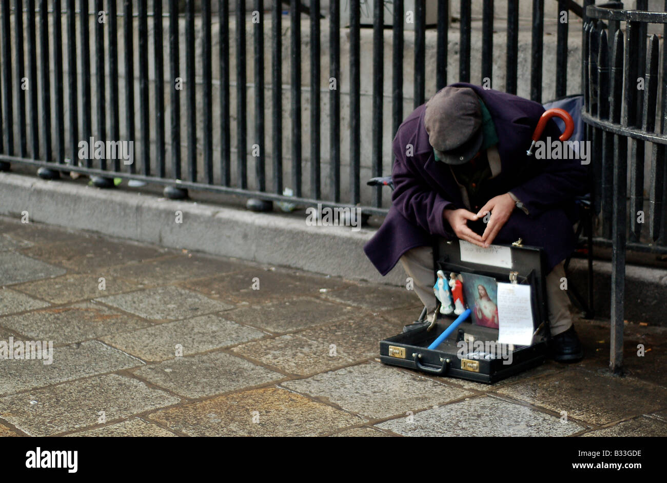 Ein älterer Mann sitzt in der Kälte des Winters, Verkauf von Kleinteilen Passanten außerhalb einer Kirche im Zentrum von Dublin. Stockfoto