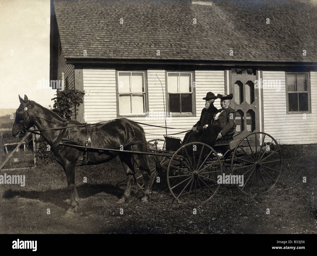 Ca. 1931 antikes Foto von einem älteren Ehepaar in ihrem Pferd und Buggy vor ihren Bauernhof Haus, wahrscheinlich Maine, USA. Stockfoto