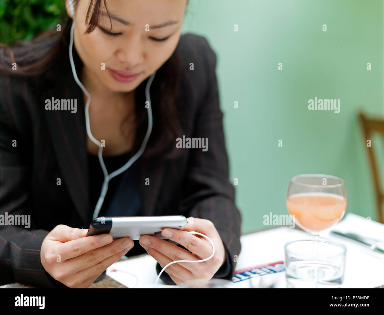 Eine junge Frau hört ihr Mobiltelefon während der Blick auf dem Bildschirm in einem Restaurant. Stockfoto