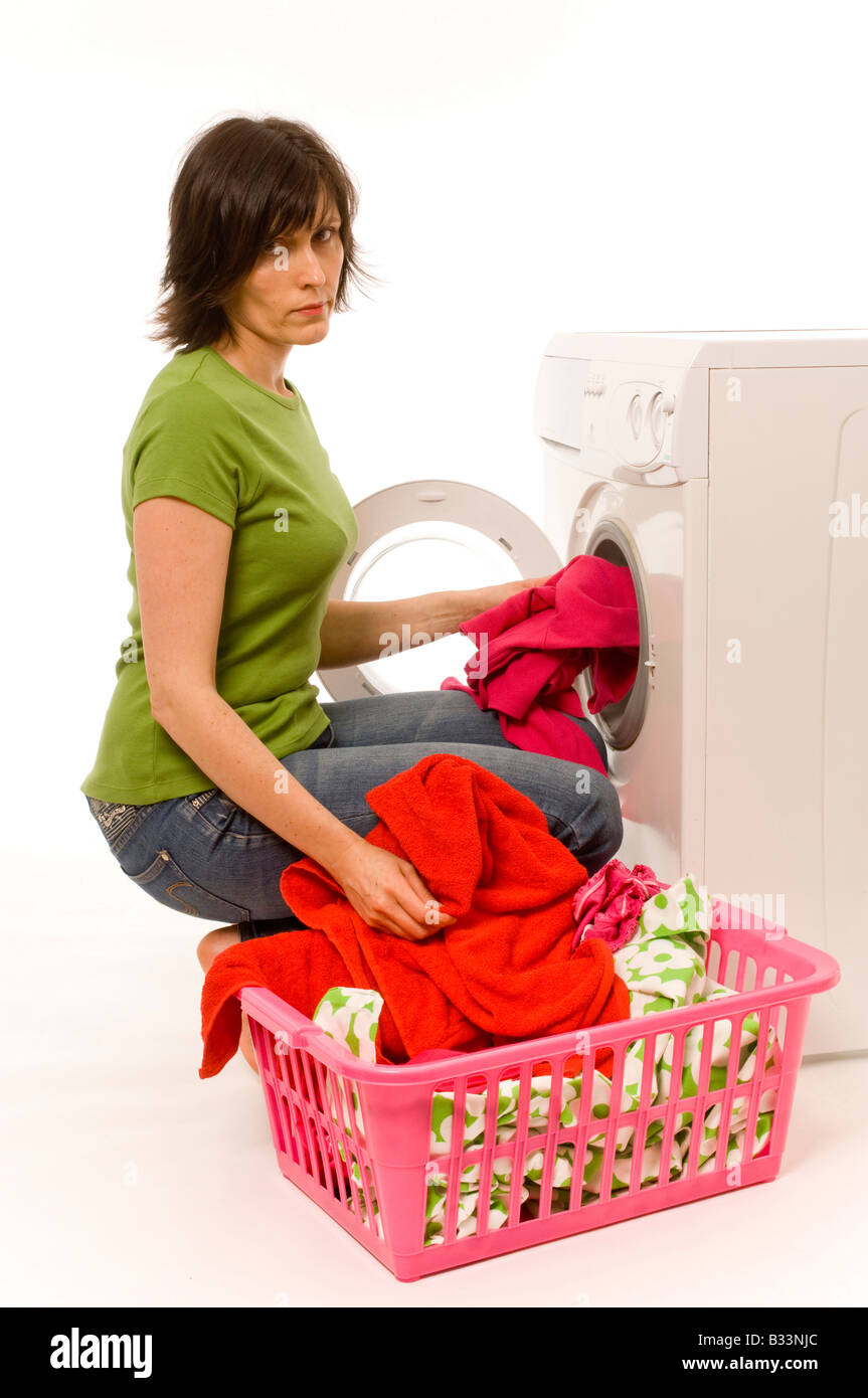 Junge weiße Frau mit einem grünen T-Shirt und Jeans, die Haushaltswaschmaschine mit bunten Kleidern aus dem Wäschekorb beladen. Stockfoto