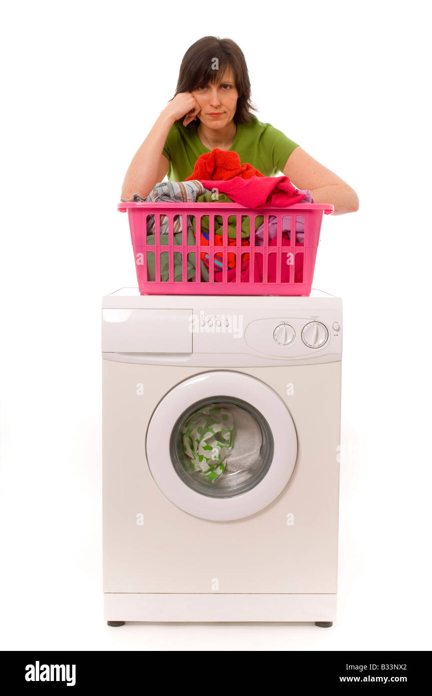 Eine trostlose junge weiße Frau, die ein grünes T-Shirt trägt und sich auf einen pinkfarbenen Wäschekorb voller Kleidung lehnt, der auf einer Waschmaschine steht Stockfoto