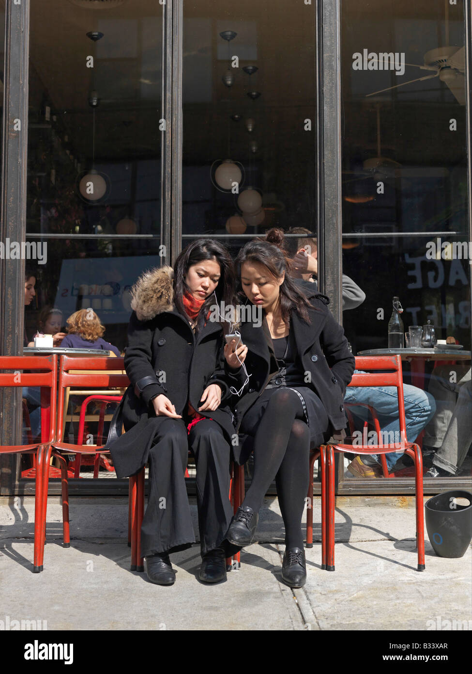Zwei junge asiatische Frauen hören Sie Musik von einem Mobiltelefon beim Lachen außerhalb eines Restaurants Stockfoto