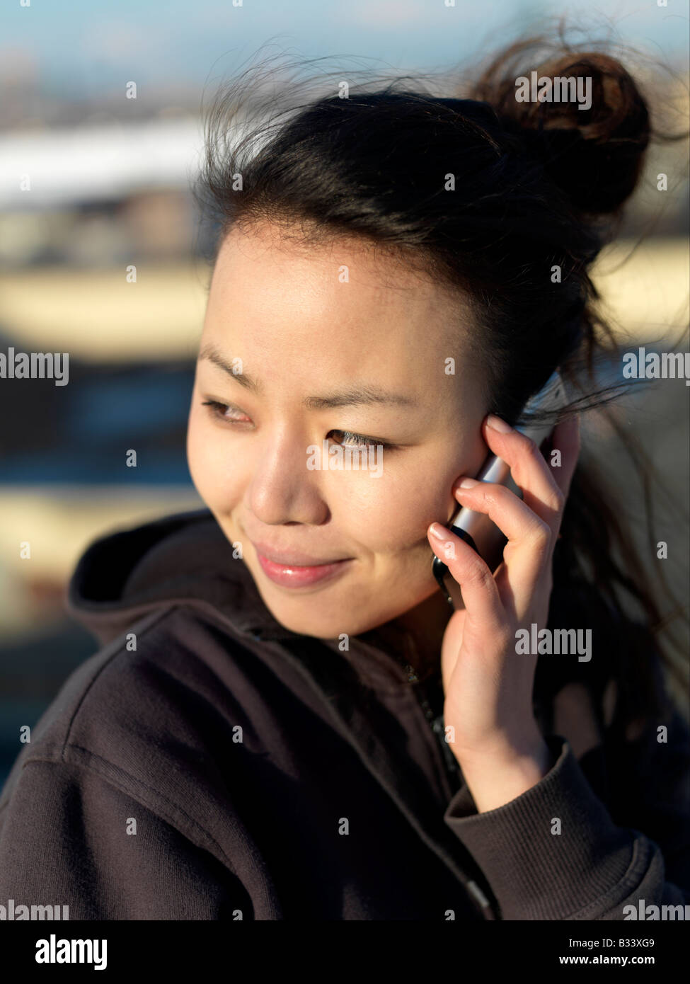 Eine junge Asiatin hört ihr Handy während lächelnd Stockfoto