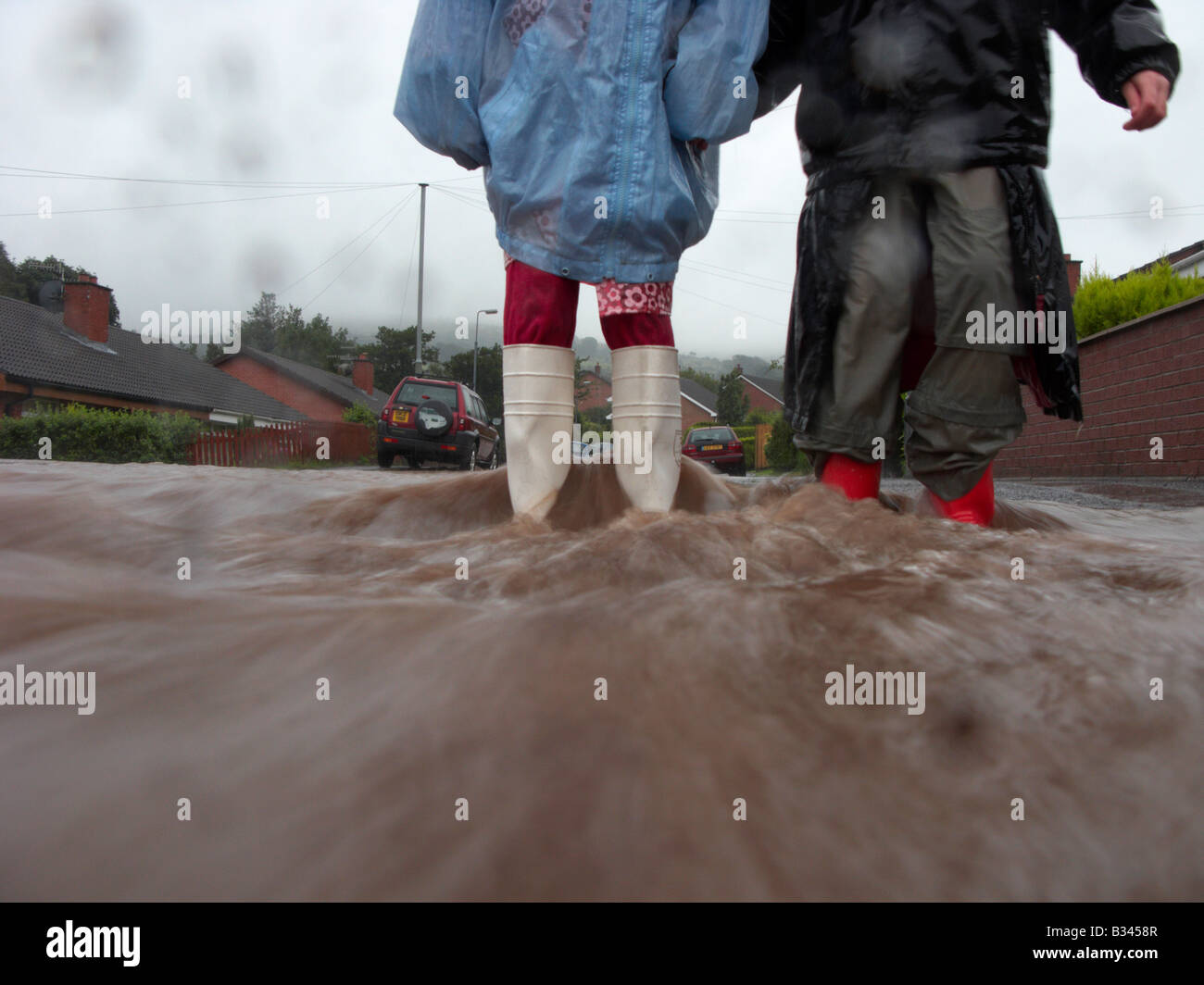 zwei junge Mädchen tragen Regenmantel und Wellington Boots im Wasser vom Regen und Fluss Überlauf Fluten einer Straße im Newtow steht Stockfoto