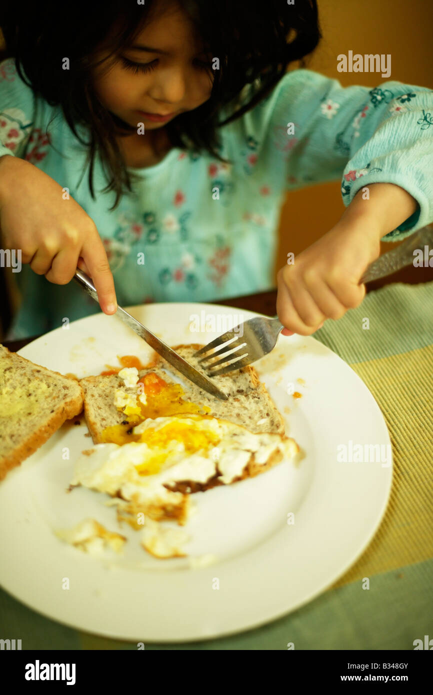 Lernen, benutzen Sie ein Messer und Gabel ein Fünf Jahres altes Mädchen isst Spiegelei auf toast Stockfoto