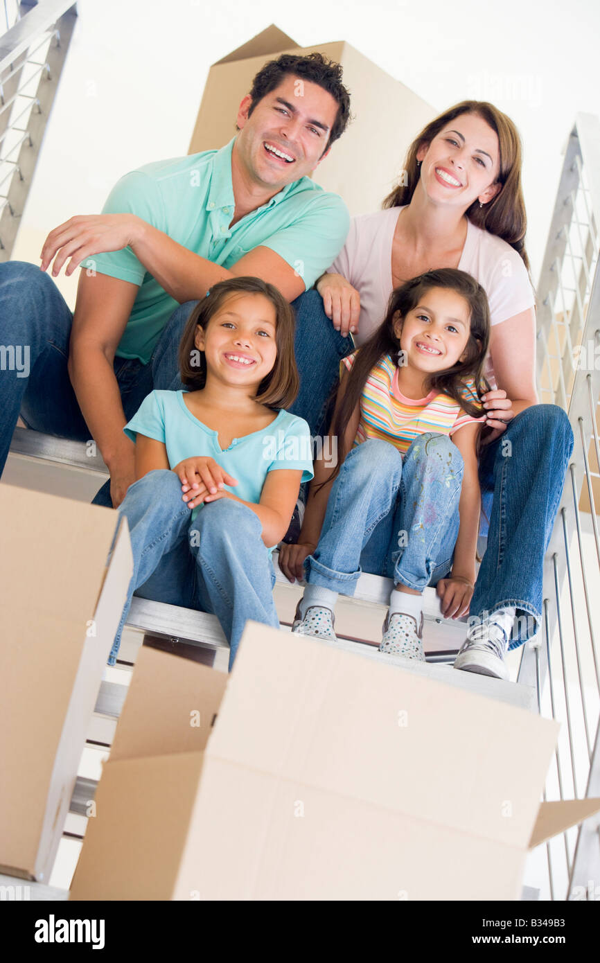 Familie sitzt auf der Treppe mit Boxen im neuen Hause lächelnd Stockfoto