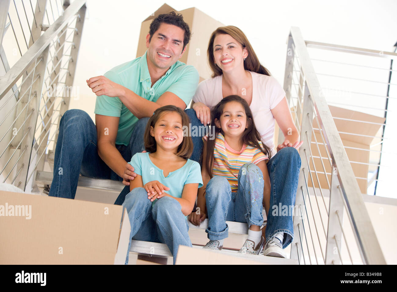 Familie sitzt auf der Treppe mit Boxen im neuen Hause lächelnd Stockfoto