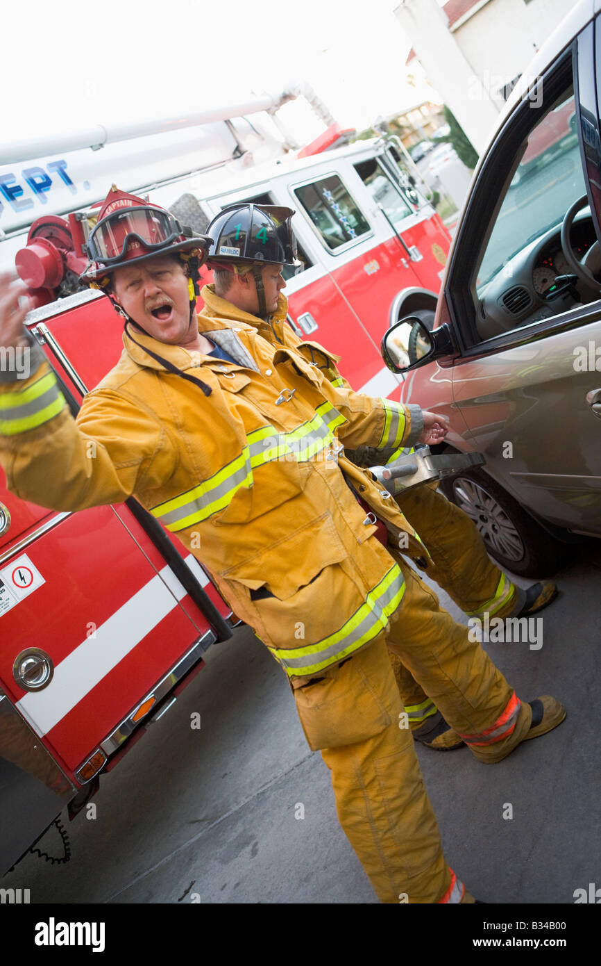 Feuerwehrmann deutete für die Sicherung mit einem anderen Feuerwehrmann über die Backen des Lebens auf einer Autotür (Blur) Stockfoto