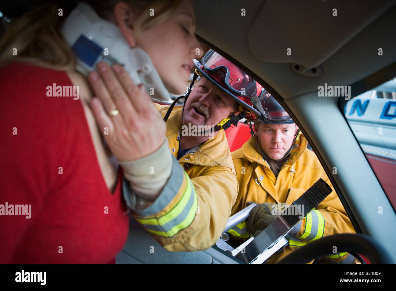 Feuerwehrmann hilft Frau mit Nackenschutz, während ein anderer Feuerwehrmann die Backen des Lebens auf einer Autotür (Tiefenschärfe verwendet) Stockfoto
