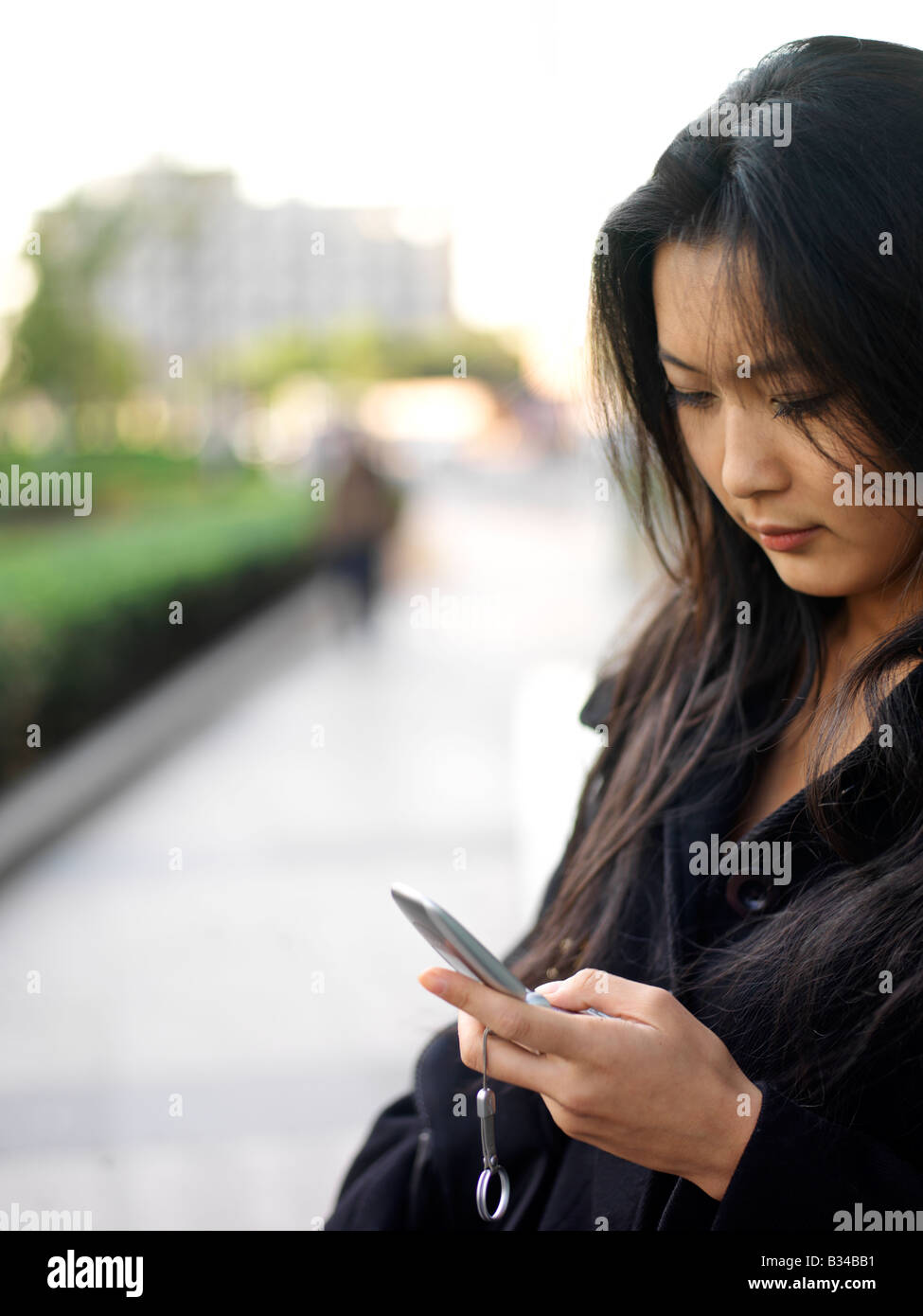 Eine junge chinesische Geschäftsfrau mit ihrem Handy in der Stadt Stockfoto