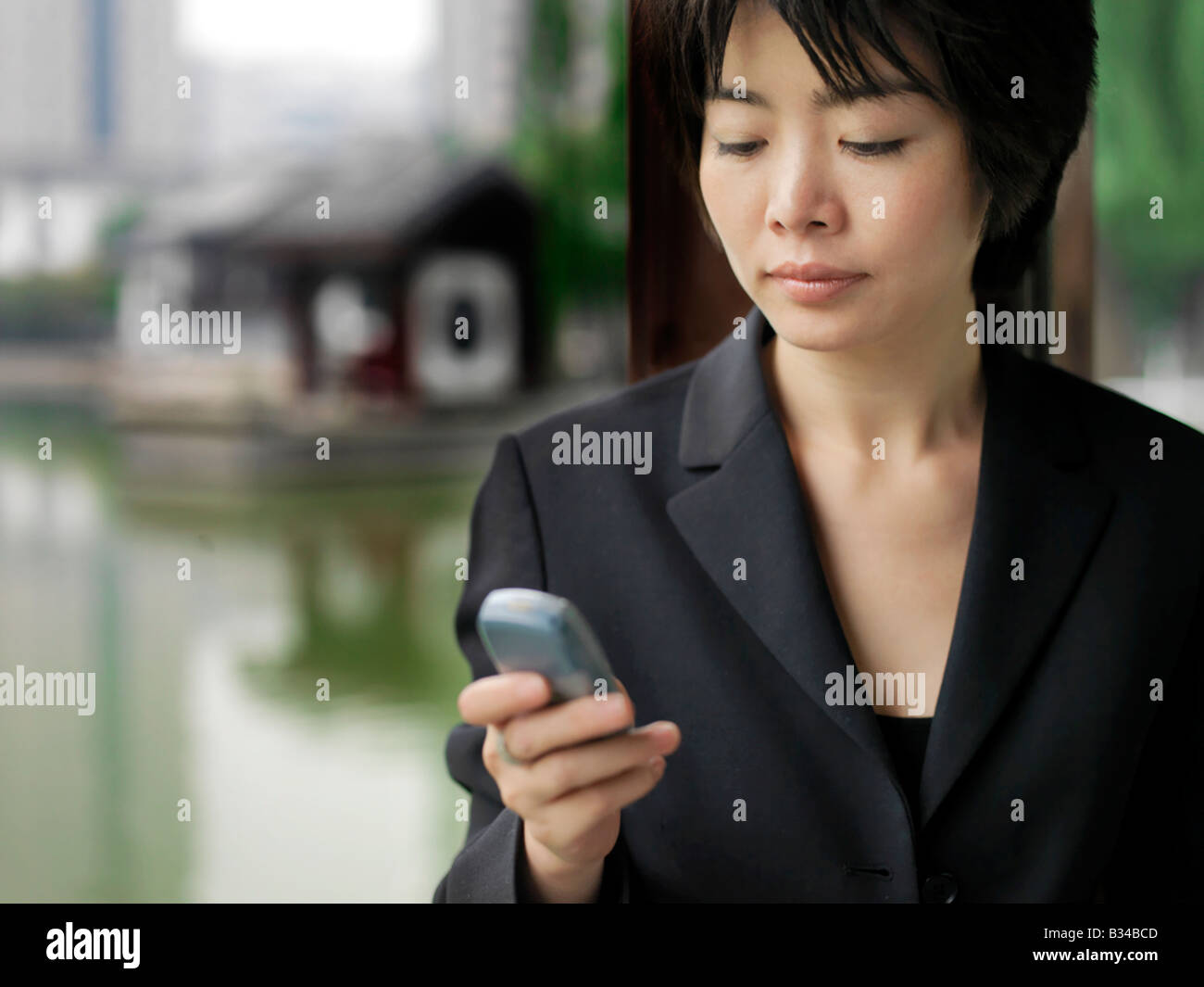 Eine chinesische Geschäftsfrau mit ihrem Mobiltelefon mit chinesischer Architektur im Hintergrund. Stockfoto