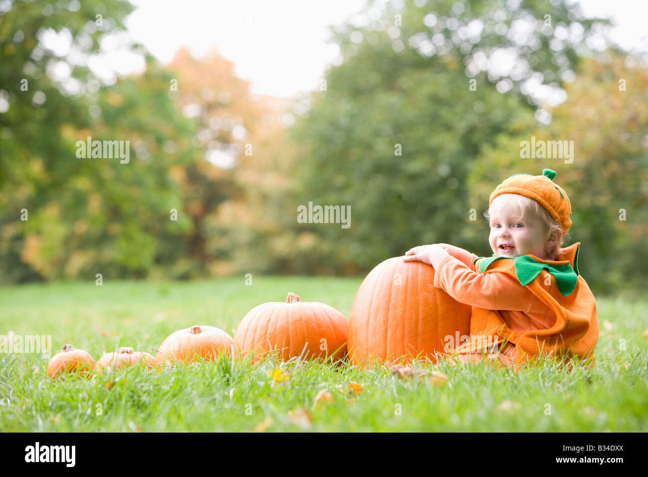 Baby Boy im Freien in Kürbiskostüm mit echten Kürbisse Stockfoto