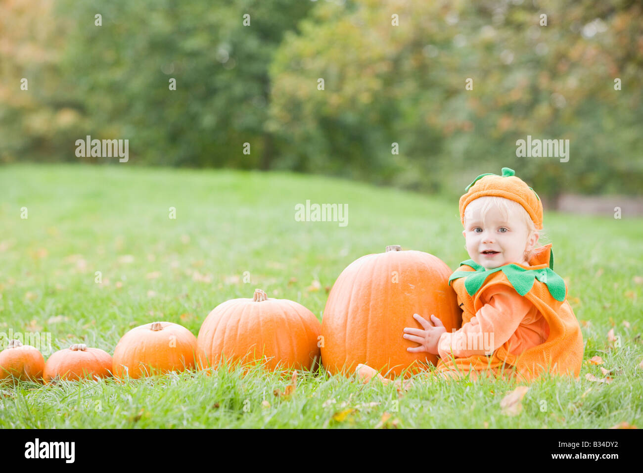 Baby Boy im Freien in Kürbiskostüm mit echten Kürbisse Stockfoto