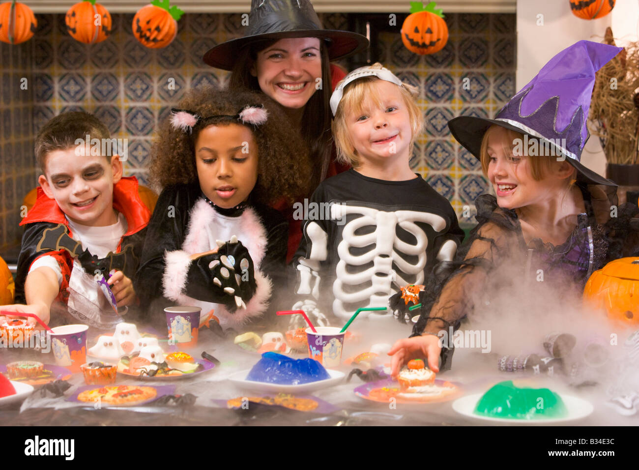 Vier junge Freunde und eine Frau an Halloween essen Leckereien und lächelnd Stockfoto