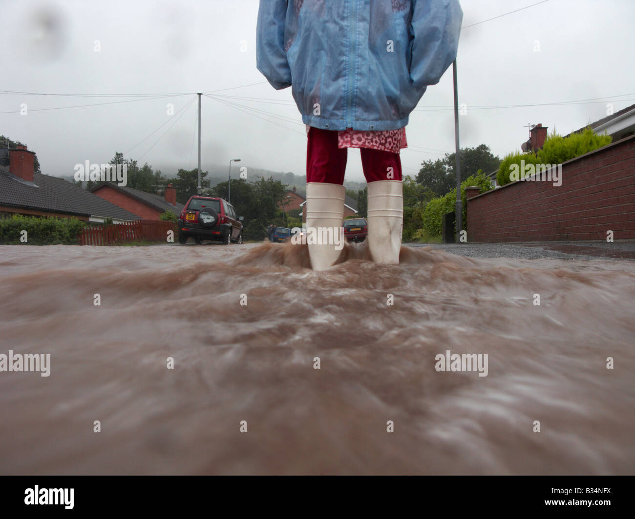 junge Mädchen tragen Regenmantel und Wellington Stiefel stehen im Wasser vom Regen und Fluss Überlauf Überschwemmungen Straße Herzinfarkt Stockfoto