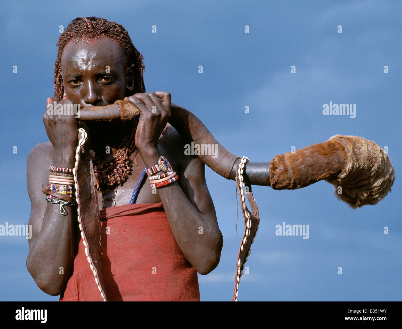 Kenia, Trans-Mara, Lolgorien. Ein Massai-Krieger bläst eine Trompete aus dem Horn eine große Kudu umgearbeitet. Der Gurt ist mit Kaurimuscheln verziert. Kudu-Horn-Trompeten sind nur Klang, um Männer zu den Waffen oder bei feierlichen Anlässen zu nennen. Stockfoto