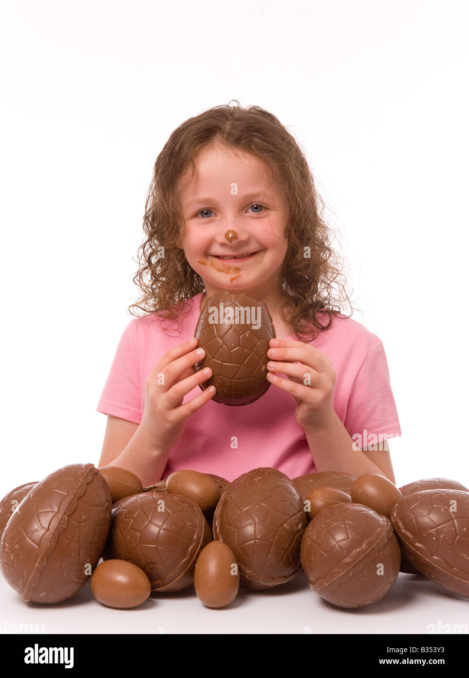Ein lächelndes Kind mit Schokolade im Gesicht, das ein Stück Ostern mit vielen Ostereiern im Vordergrund hält. Stockfoto