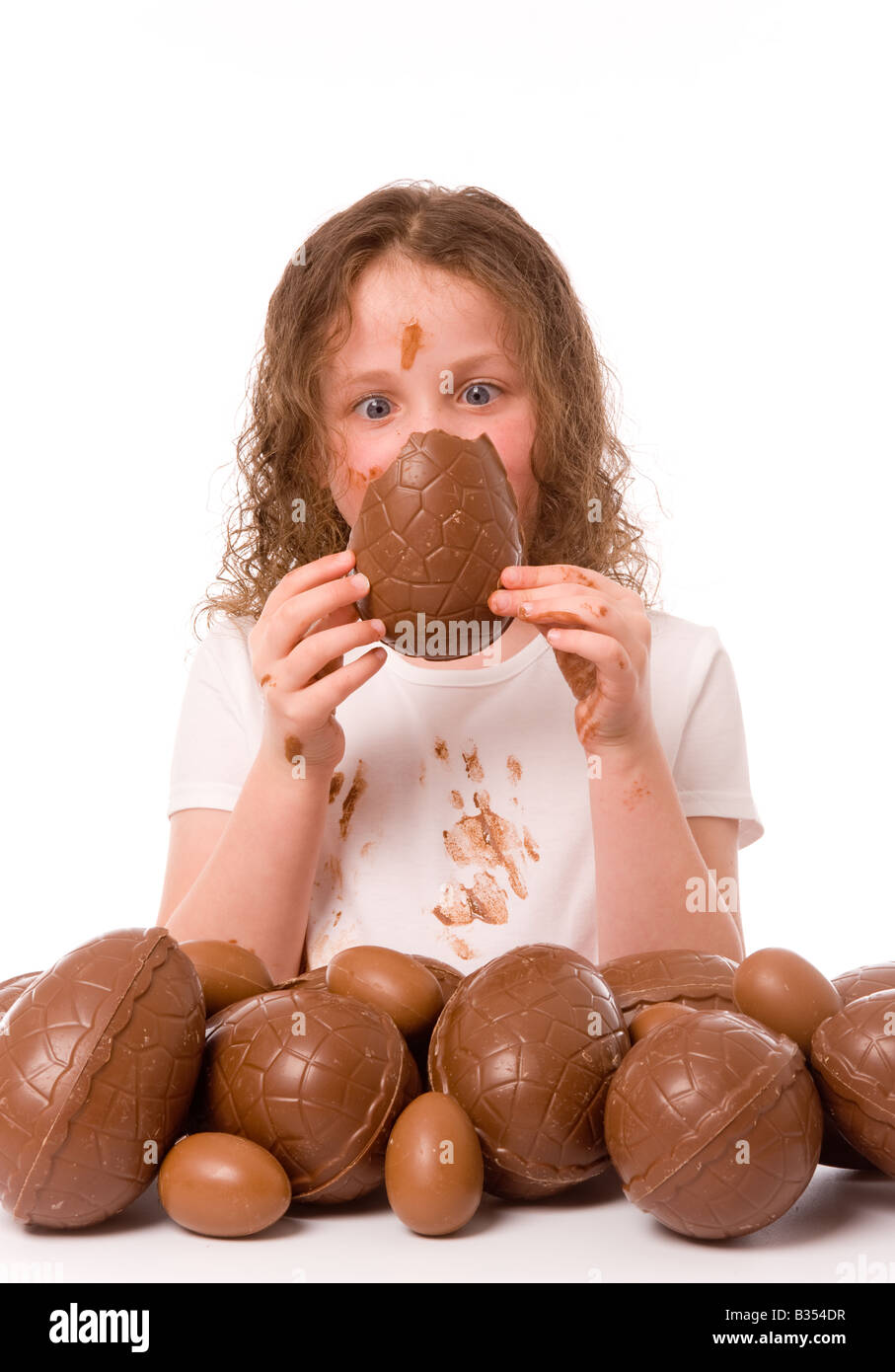 Ein kleines Kind starrt auf ein Stück Osterei, das sie vor ihrem mit Schokolade bedeckten Gesicht hält. Stockfoto