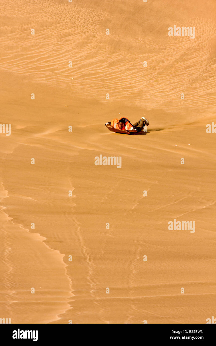 Eine lokale Mann Notfallblitzers durch Abrutschen einer Sanddüne auf einer polierten Tafel in der Nähe von Swakopmund eine Stadt an der Atlantikküste Namibias. Stockfoto
