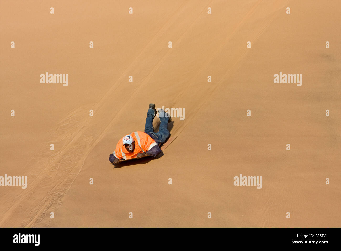 Eine lokale Mann Notfallblitzers durch Abrutschen einer Sanddüne auf einer polierten Tafel in der Nähe von Swakopmund eine Stadt an der Atlantikküste Namibias. Stockfoto