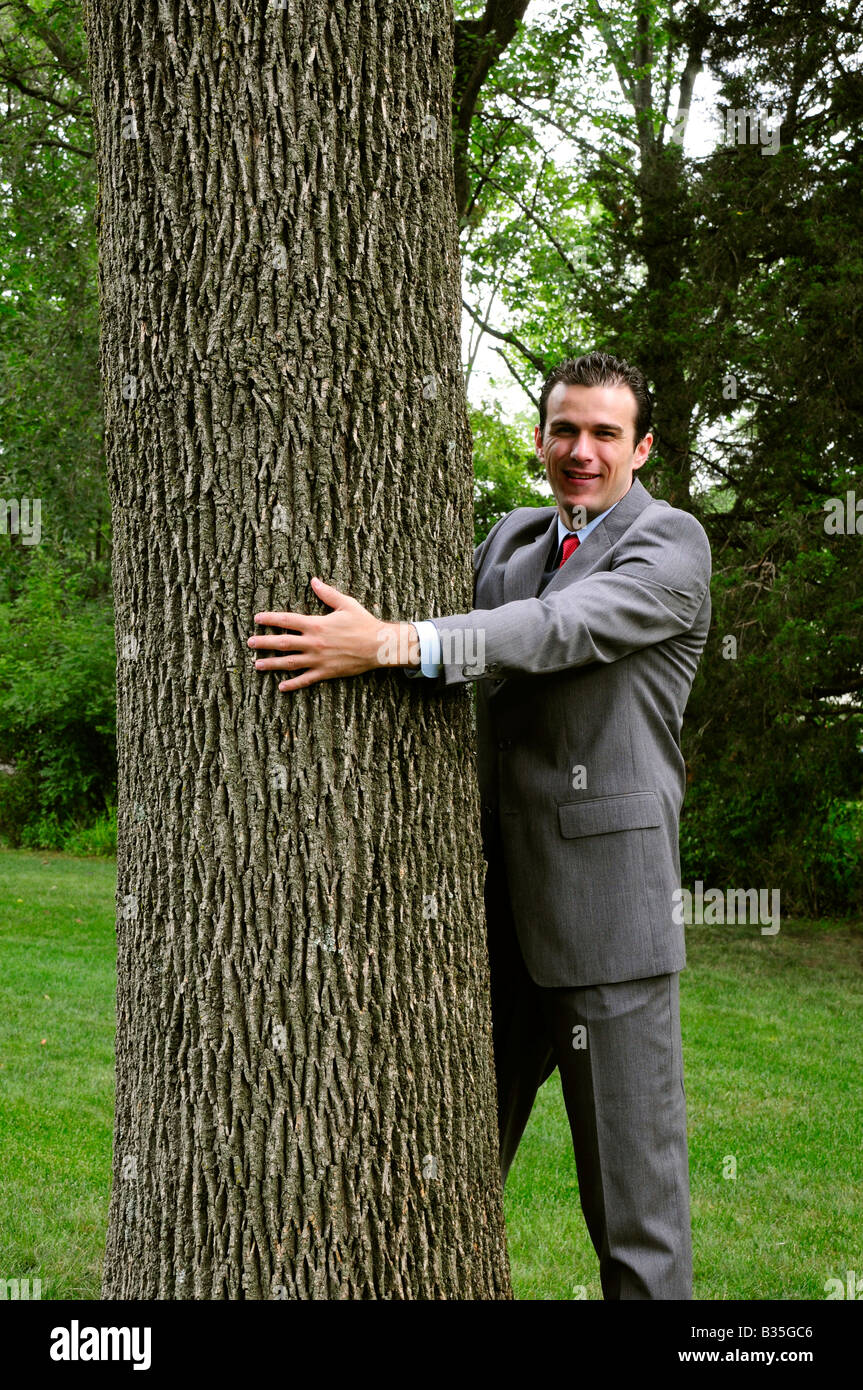 Ein Geschäftsmann im Anzug umarmt einen Baum, Treehugger corporate Umweltschutz darstellt Stockfoto
