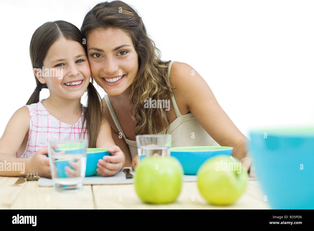 Mutter und Tochter sitzen Wange an Wange am Tisch, beide Lächeln in die Kamera Stockfoto