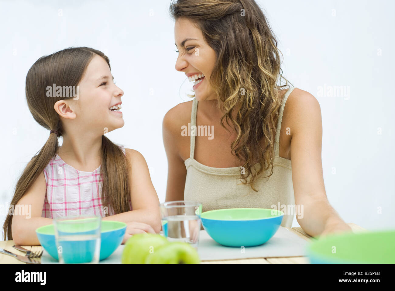 Mutter und Tochter sitzen am Tisch, lachen einander an Stockfoto