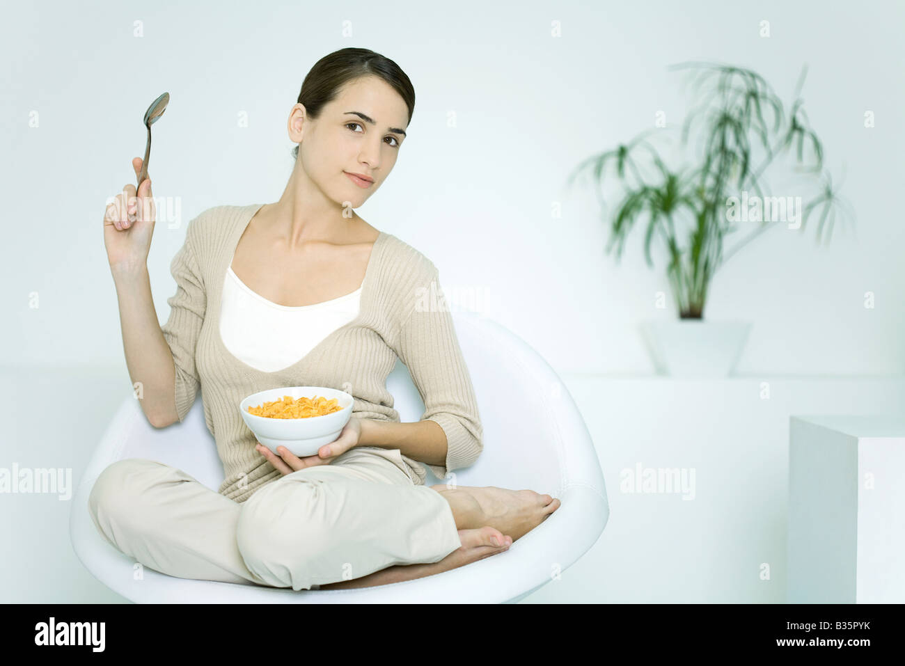Junge Frau sitzt im Stuhl halten Müslischale und Löffel, lächelnd in die Kamera Stockfoto