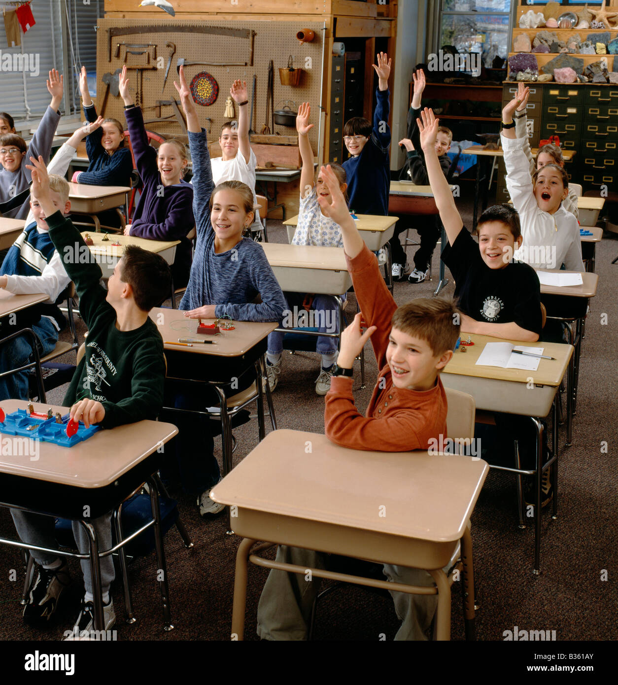 Grundschüler erheben begeistert ihre Hände in Beantwortung der Frage des Lehrers Stockfoto
