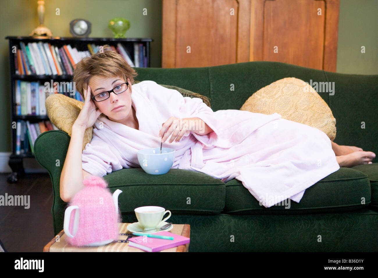 Junge Frau auf Sofa zu Hause essen eine süße Leckerei Stockfoto
