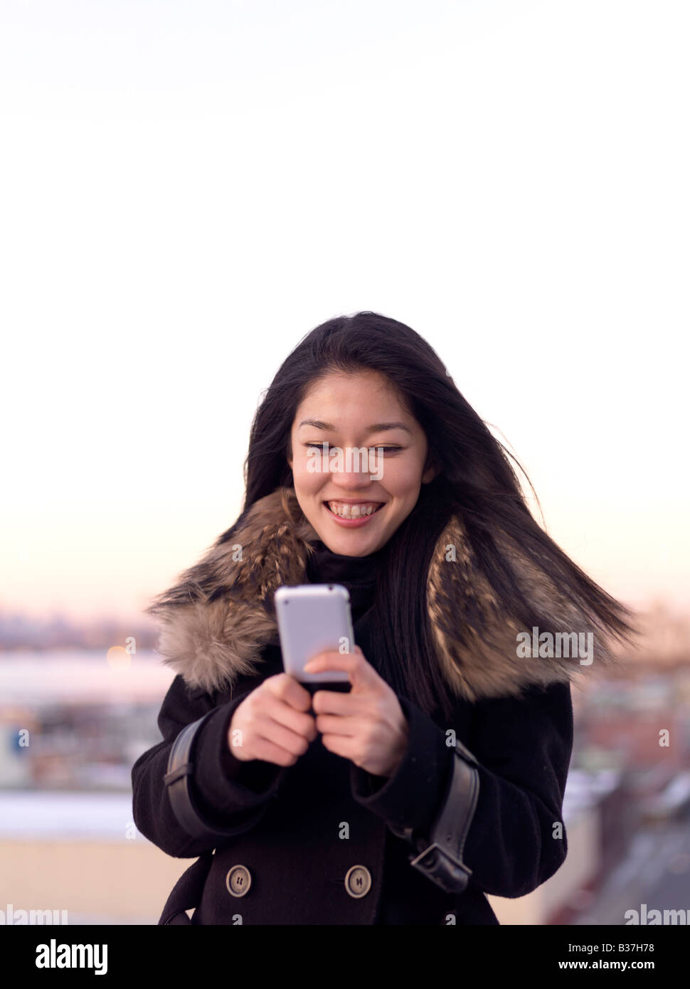 Eine junge Frau stehen im freien Lächeln, wie sie etwas auf ihrem Handy liest. Stockfoto