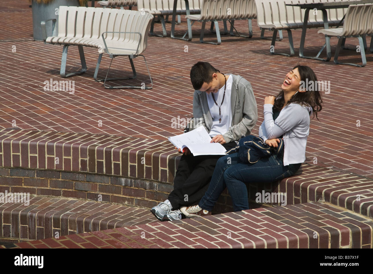Eine junge Dame, die lachend sitzen auf Stufen mit ihrem Freund in der Barbican Estate City of London Stockfoto