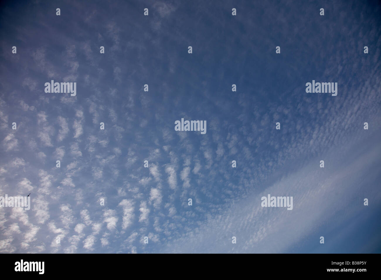 Altocumulus Wolken gegen ein Reich blauer Himmel und eine winzige bekommen Ranger Bell 206 Hubschrauber Stockfoto
