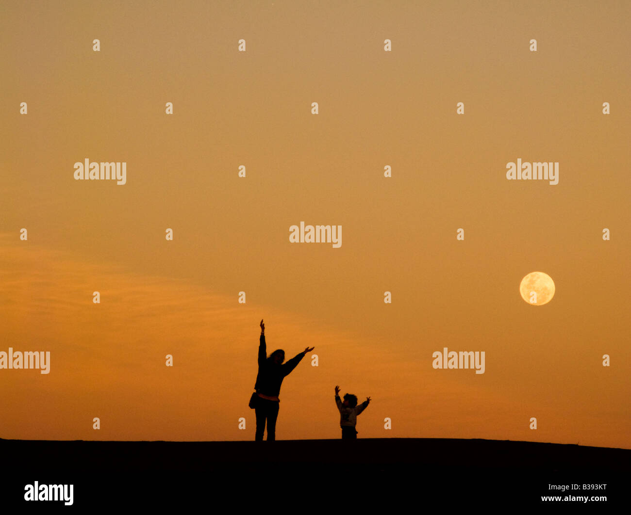 Kinder gehen auf einer Düne mit einem riesigen Mond Stockfoto