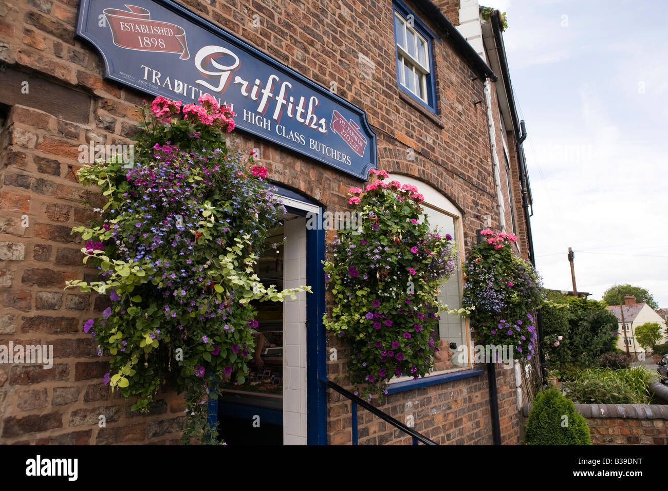 UK Cheshire Farndon High Street Blumen Blumenampeln außerhalb Griffiths traditionellen Metzger-shop Stockfoto