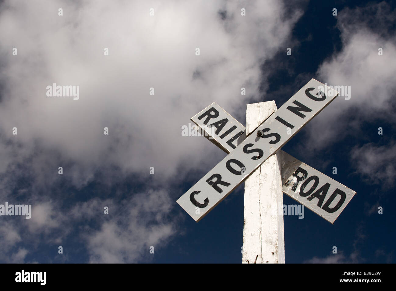 Railroad Crossing Zeichen auf einem weiß getünchten Mast vor einem dunklen blauen Himmel mit Wolken Stockfoto