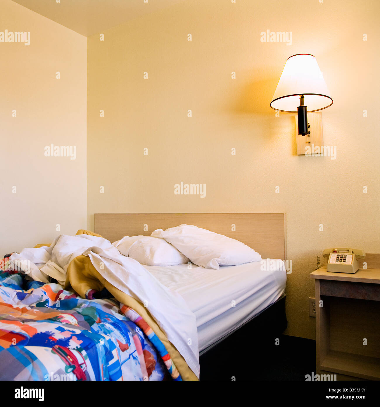 Innenaufnahme der Motelzimmer mit ungemachten Bett und Wandleuchte Stockfoto