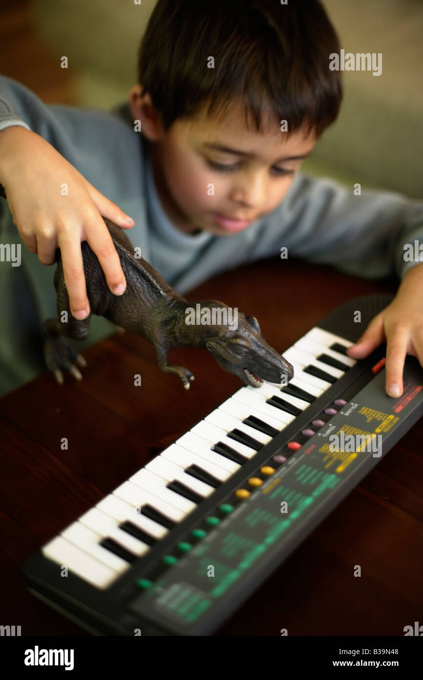 T Rex spielt Notizen sechs Jahre alter Junge verwendet Spielzeug Tyrannosaurus Rex, Noten am e-Piano zu spielen Stockfoto