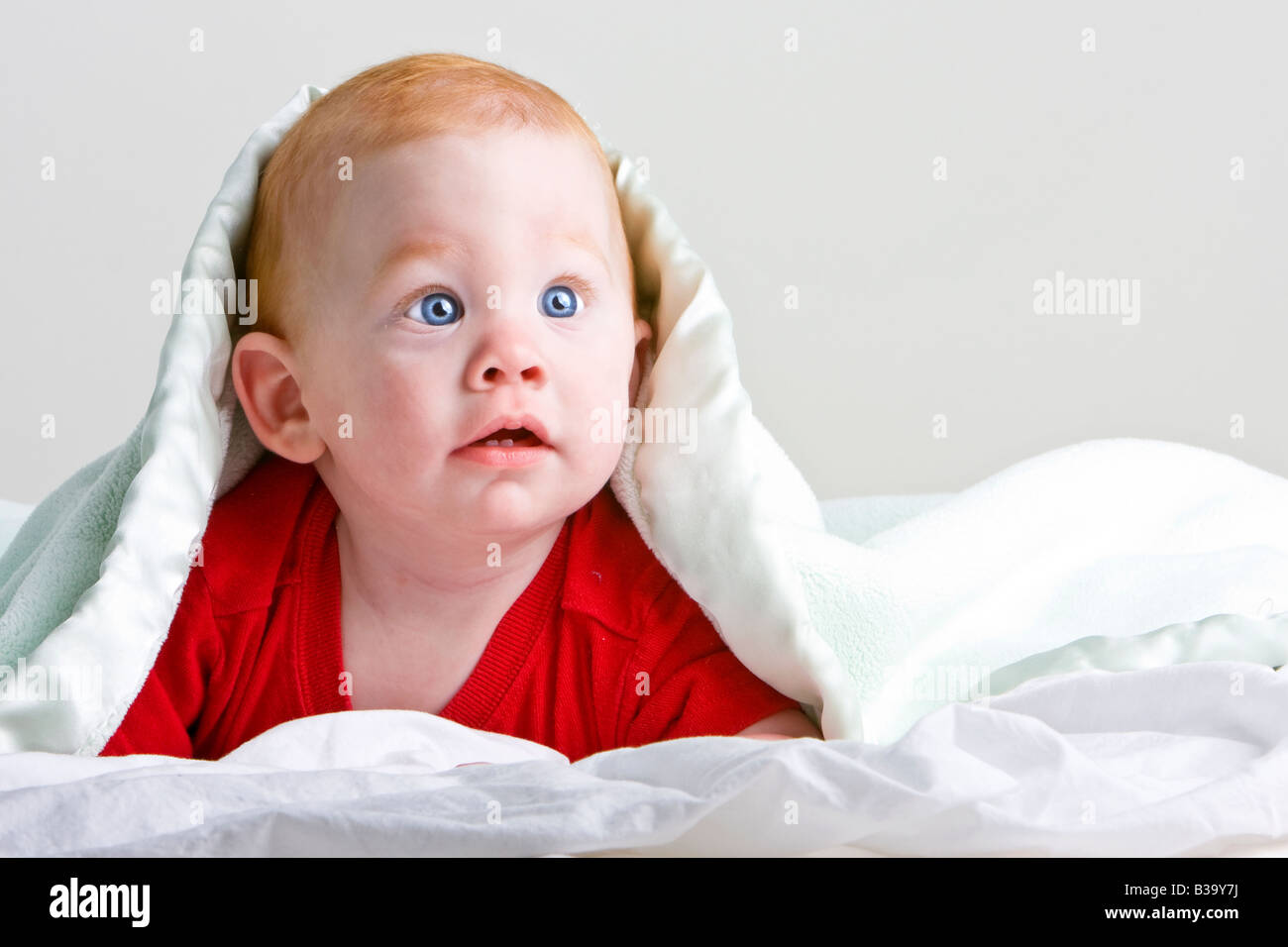 Schöne junge Baby mit roten Haaren auf Front unter weichen Decke liegend Stockfoto