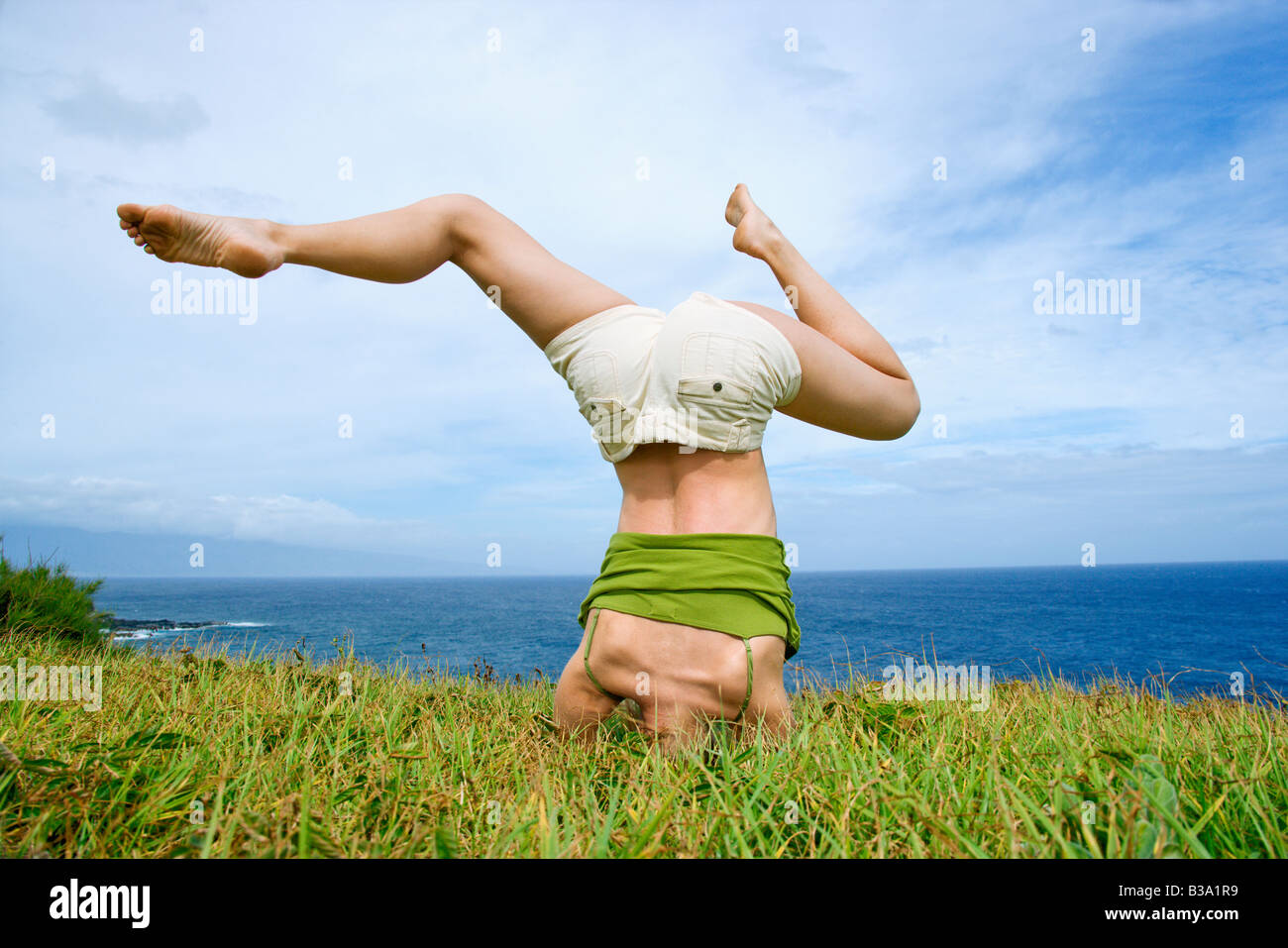 Junge Frau macht Kopfstand mit Beinen schief Gras in der Nähe von Meer in Maui Hawaii Stockfoto