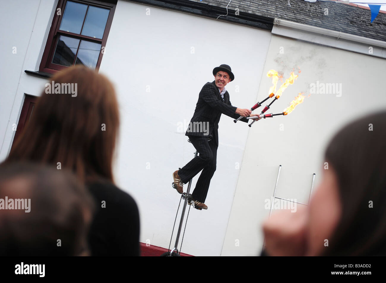 A Street Performer Entertainer sticks Einradfahren und Jonglieren mit Feuer in Lostwithiel, Cornwall, UK Stockfoto