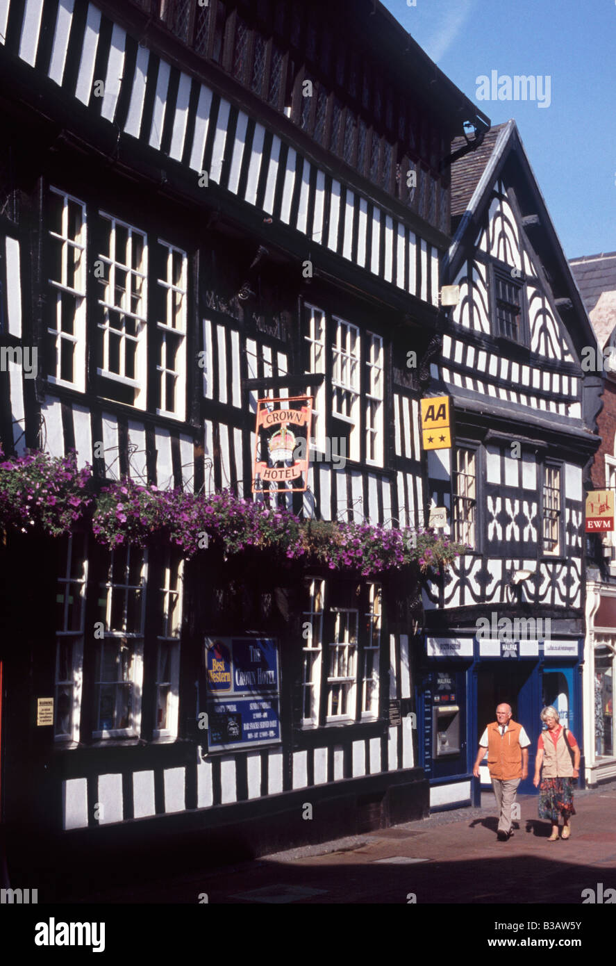 Älteres paar Walkiing an Nantwich High Street vor schwarzen und weißen Holz Rahmen Hotels und Geschäfte, Nantwich, Cheshire Stockfoto