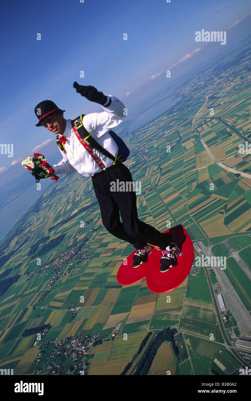 Ein Fallschirmspringer mit Anzug und Hut surft auf einem herzförmigen  Surfbrett In seiner linken Hand er s hält einen Blumenstrauß  Stockfotografie - Alamy