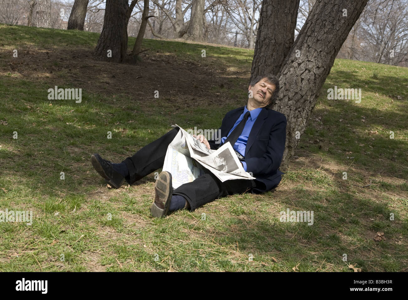 Erschöpft von der Suche nach Arbeit Mann in seinen frühen sechziger Jahren ruht unter einem Baum im park Stockfoto