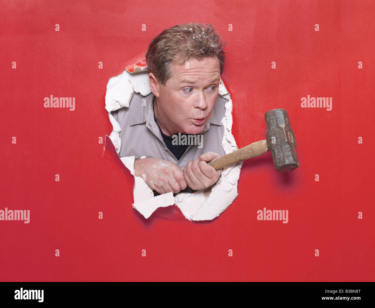 Mann bricht durch die Wand mit Vorschlaghammer Stockfoto
